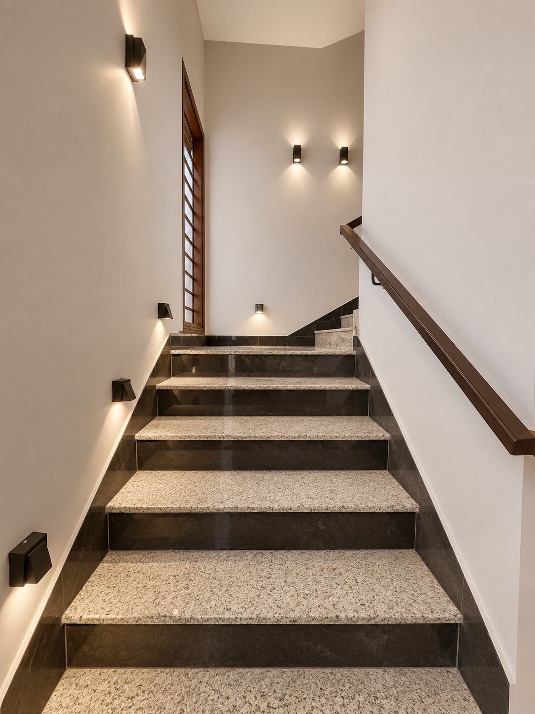 Granite staircase with wood handrail and accent wall lighting